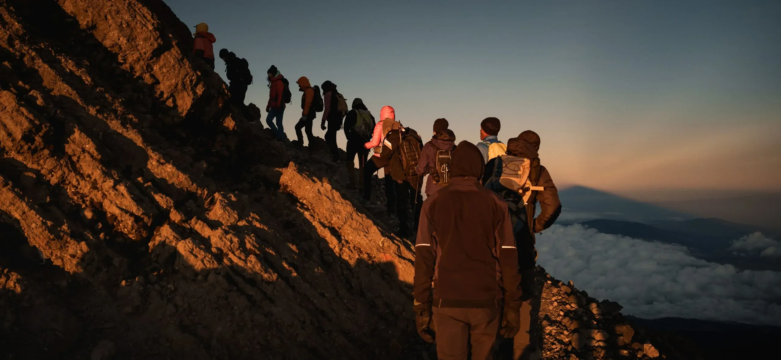 A line of climbers on Mount Kilimanjaro's summit ridge at sunrise, above the clouds