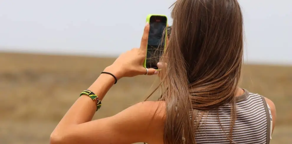 Woman with long hair taking a photo with her smartphone in an open landscape.